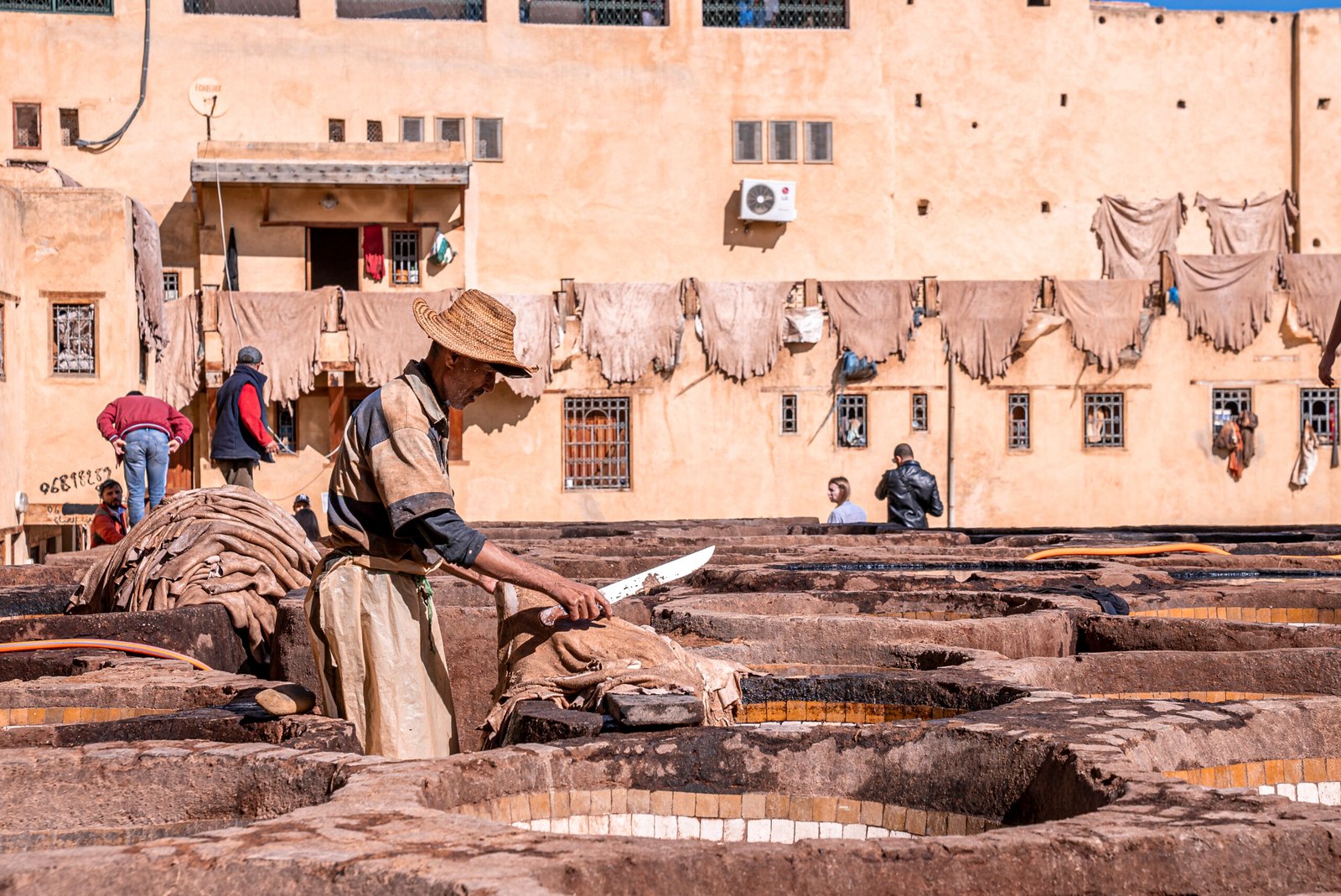 Fes, Morocco. October 10, 2021. Man cutting leather with knife at tannery next to brims of old stone water baths